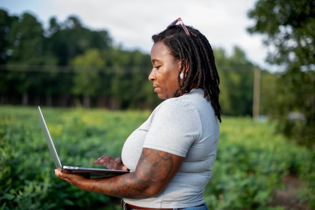 Woman using laptop in a farm field, demonstrating remote farm monitoring and digital agriculture management